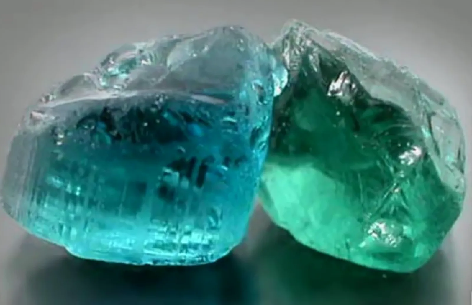 Two rough beryl stones side by side, one blue aquamarine and one green emerald.