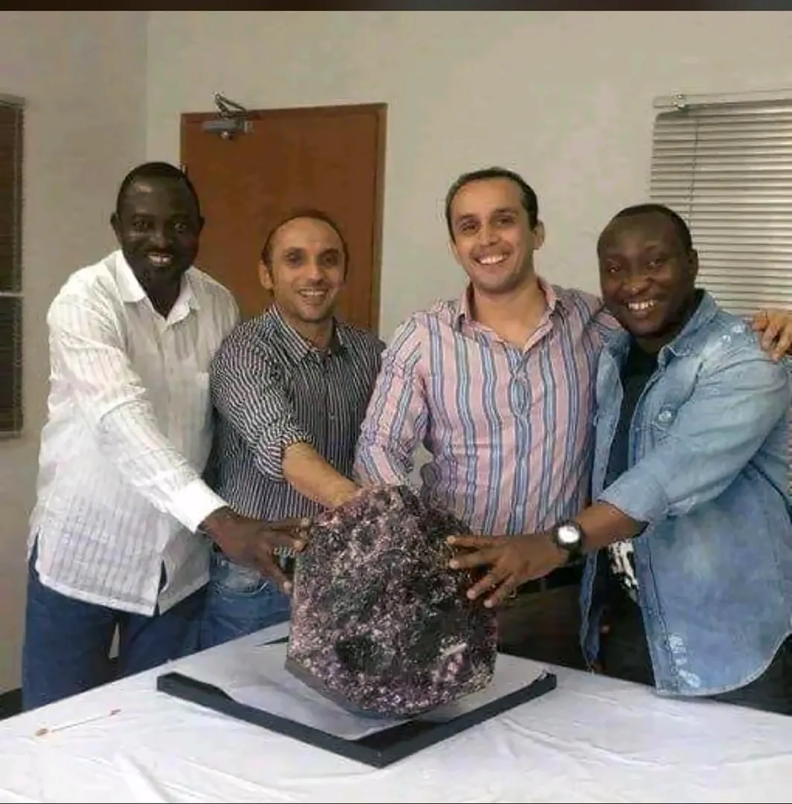 The managing director of NASAUDE International Mining with three colleagues, hands resting on a large uncut amethyst specimen on a display table.
